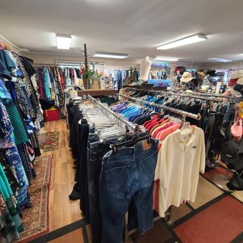 Thrift store with racks of colorful clothes and jeans under bright lights.