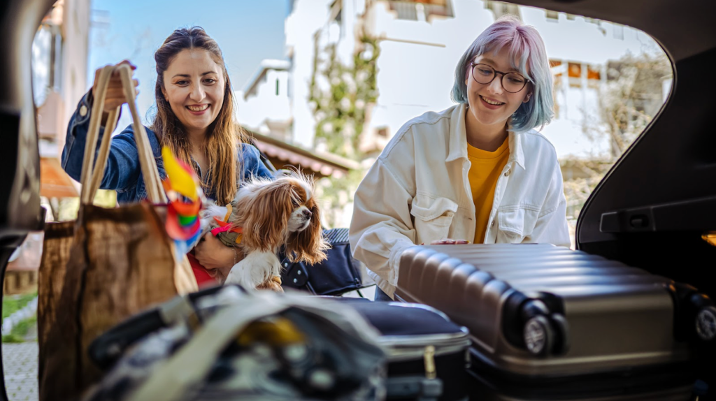 Sustainable road trip: Friends loading car trunk with luggage and  thrifted travel essentials alongside their dog.