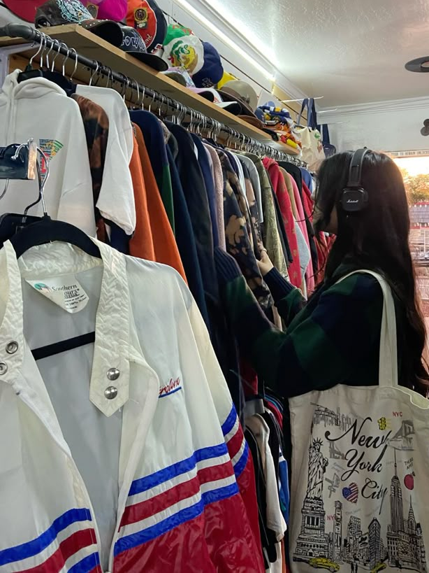 A woman with headphones shops for vintage jackets at a thrift store.