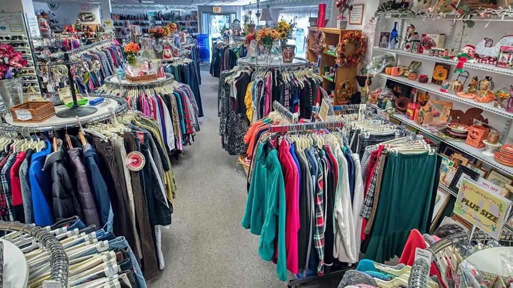 Thrift store racks are packed with colorful second-hand jackets, shirts, sweaters, and home decor.